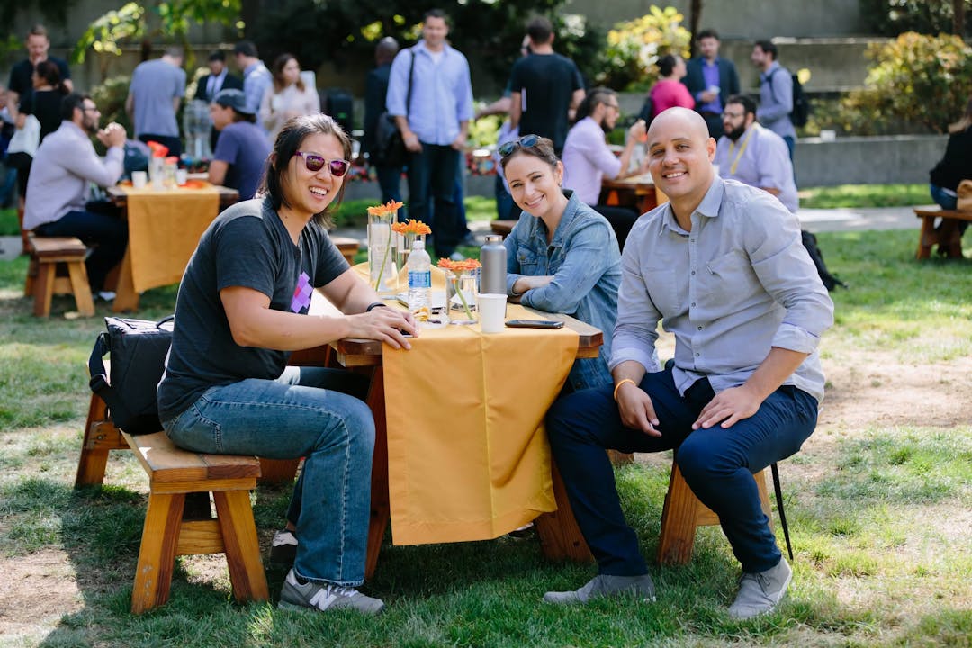 Three members of the Meadow cannabis retail software team smiling at an outdoor picnic table