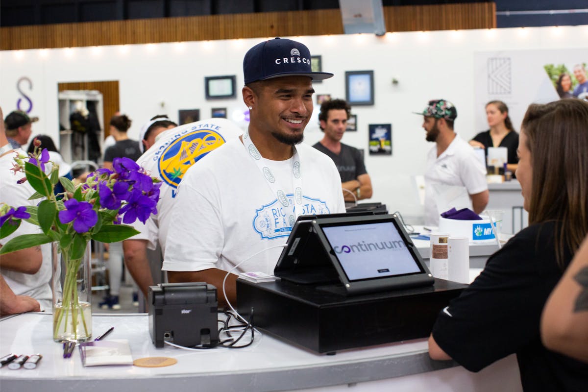 A man behind a Meadow POS station talks to a customer at a cannabis event
