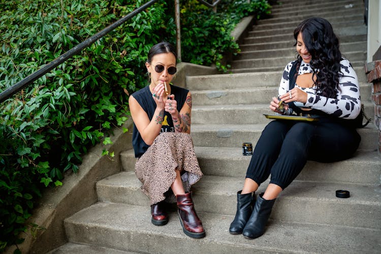 Two women smoke together outside on steps