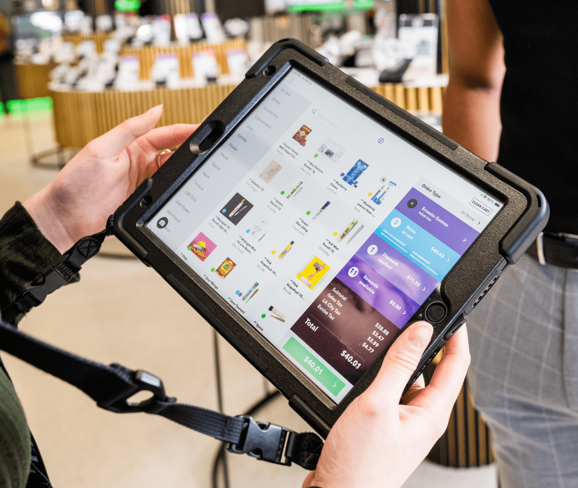 A close-up of Meadow’s cannabis POS system displayed on a tablet in a budtender's hands. The screen shows product categories, live inventory, and a checkout screen with subtotal, taxes, and payment options, illustrating Meadow’s mobile flexibility and real-time sales tools.