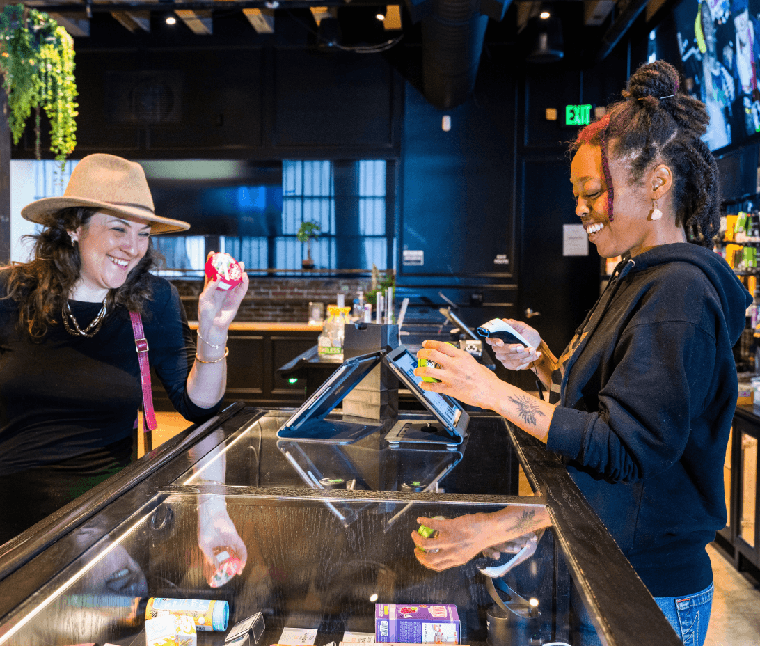 A modern, brightly-lit dispensary interior, showcasing an interaction between a dispensary team member and a smiling customer at the counter. The team member is engaged on a sleek, user-friendly interface of Meadow's software on a tablet, processing the sale efficiently. The screen displays various functionalities being utilized: processing the transaction, adding the customer to the CRM, accruing loyalty points, and capturing customer preferences for future visits. The background hints at well-organized shelves stocked with a variety of cannabis products, emphasizing the efficient inventory management. This scene embodies the seamless and integrated customer experience Meadow provides, highlighting how it simplifies business operations, ensures compliance, and enhances customer retention, all while alleviating common dispensary challenges such as product waste, regulatory complexities, and staffing issues.
A modern, brightly-lit dispensary interior, showcasing a positive interaction between a dispensary team member and a smiling customer at the counter. The team member is engaged on a sleek, user-friendly interface of Meadow's software on a tablet, processing the sale efficiently. The screen displays various functionalities being utilized: processing the transaction, adding the customer to the CRM, accruing loyalty points, and capturing customer preferences for future visits. The background hints at well-organized shelves stocked with a variety of cannabis products, emphasizing the efficient inventory management. This scene embodies the seamless and integrated customer experience Meadow provides, highlighting how it simplifies business operations, ensures compliance, and enhances customer retention, all while alleviating common dispensary challenges such as product waste, regulatory complexities, and staffing issues.